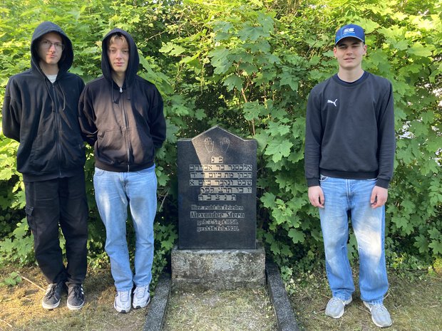 Drei Schüler beim gereinigten Grabstein von Alexander Stern (Mai 2025).