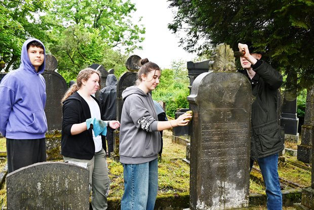 Schülergruppe beim Reinigen des Grabsteins von Jonas Bauer (Mai 2024).